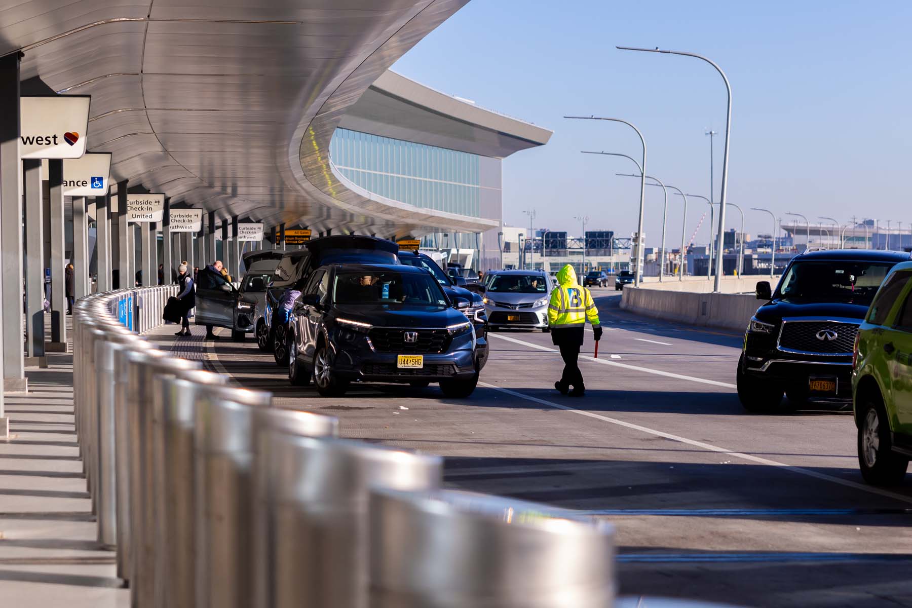 The departure gate of an airport, with a line of cars unloading travelers and luggage.