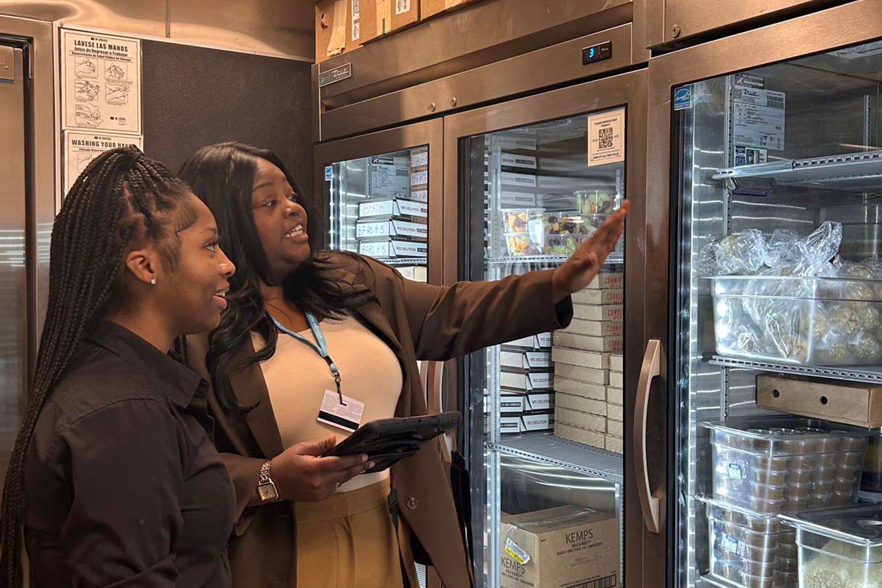 Two employees look at a cooler full of snacks and food.