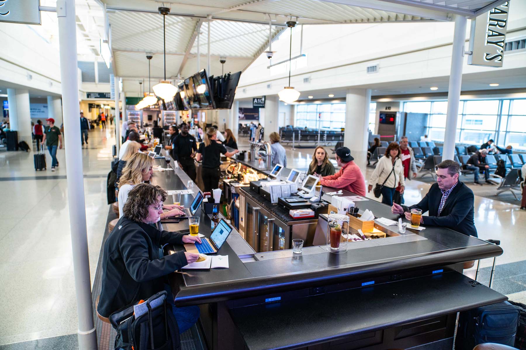 People work on laptops while sitting around an airport bar in the terminal.
