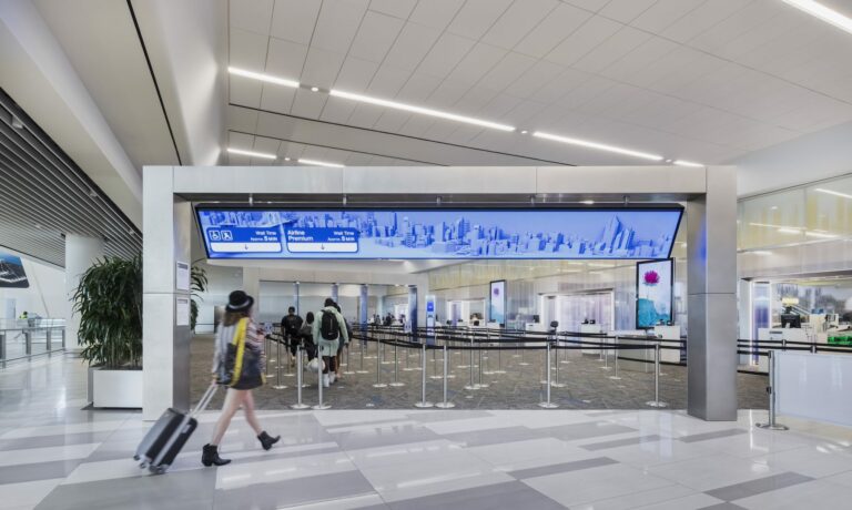 Woman approaching the security checkin point with an overarching digital display with helpful information to plan travel.
