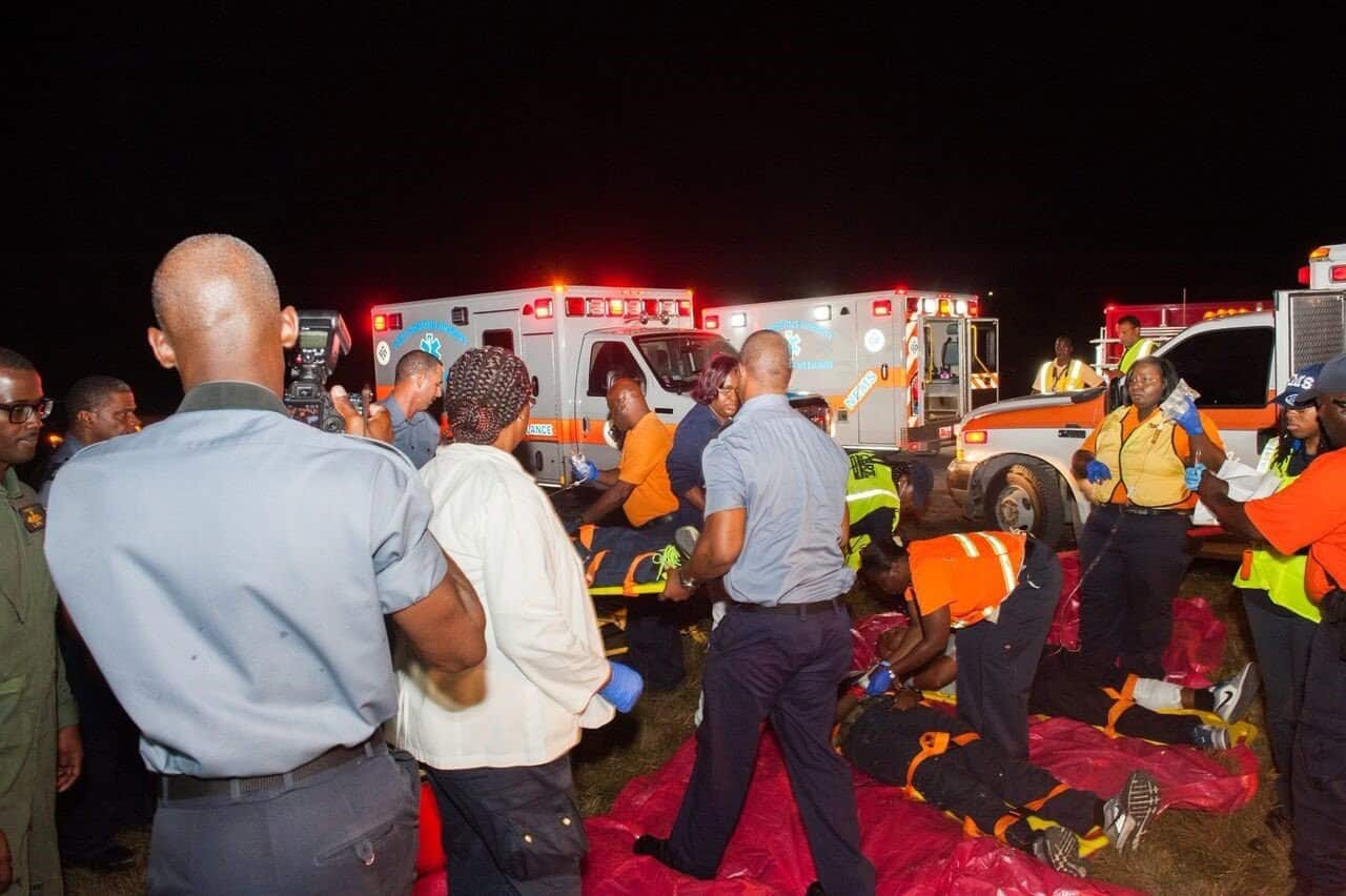 Emergency responders and bystanders at night scene with ambulances, attending to individuals on the ground.
