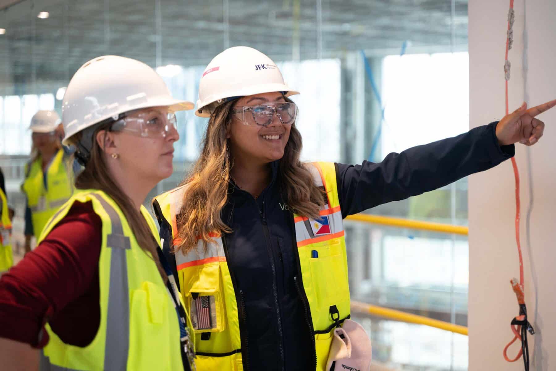 Two female construction workers on site in ppe gear pointing at progress.