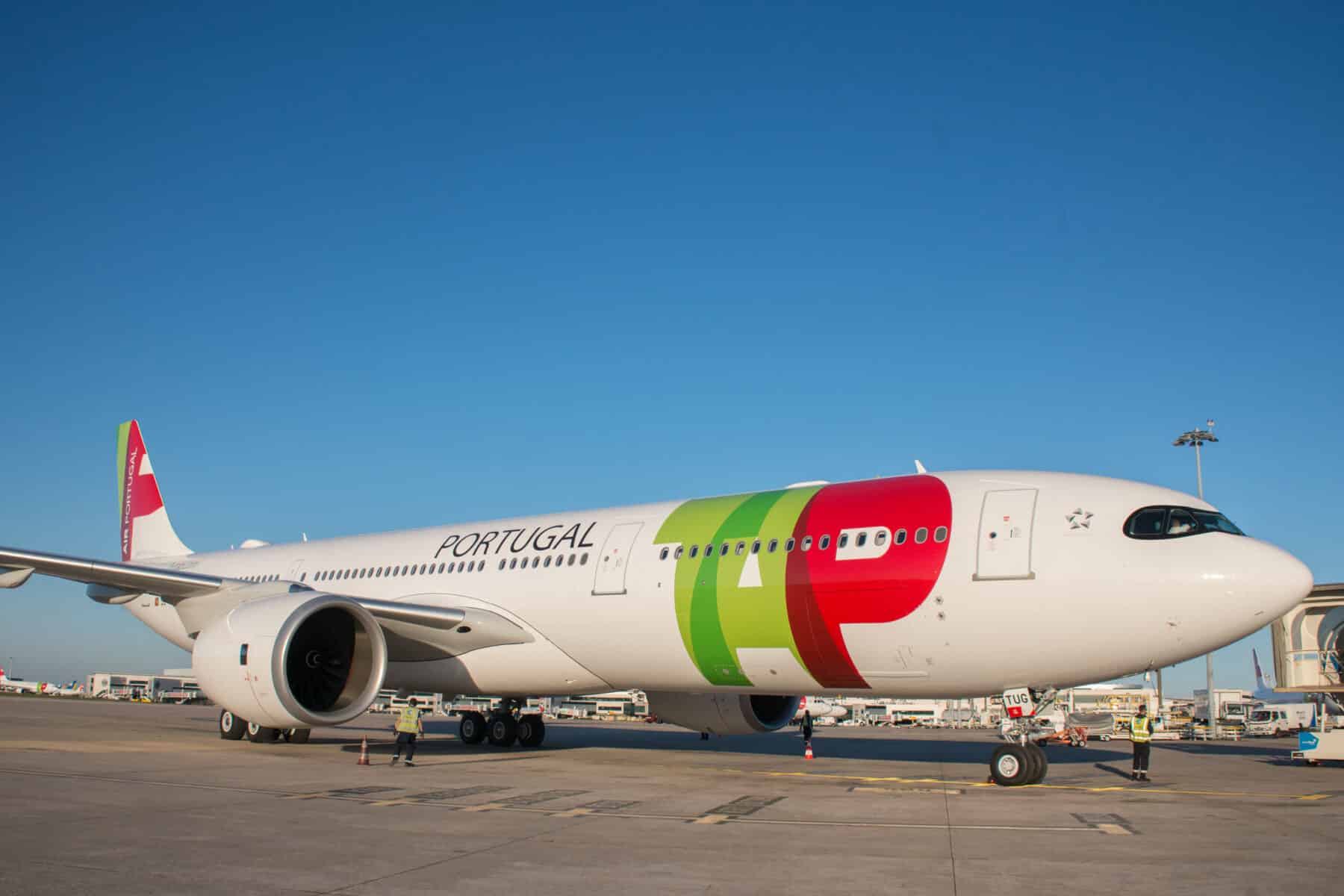 TAP Air Portugal aircraft parked on an airport tarmac under a clear blue sky.