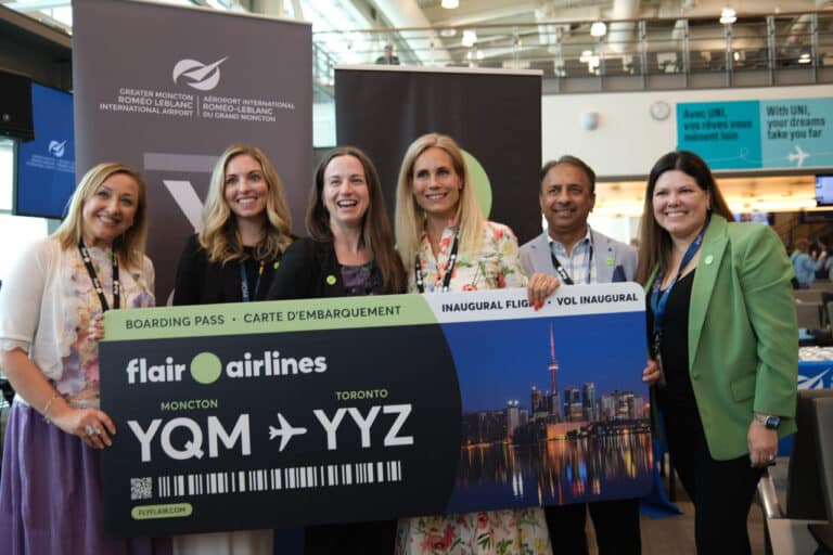 Group holding Flair Airlines inaugural boarding pass sign for Moncton to Toronto flight at Moncton Airport