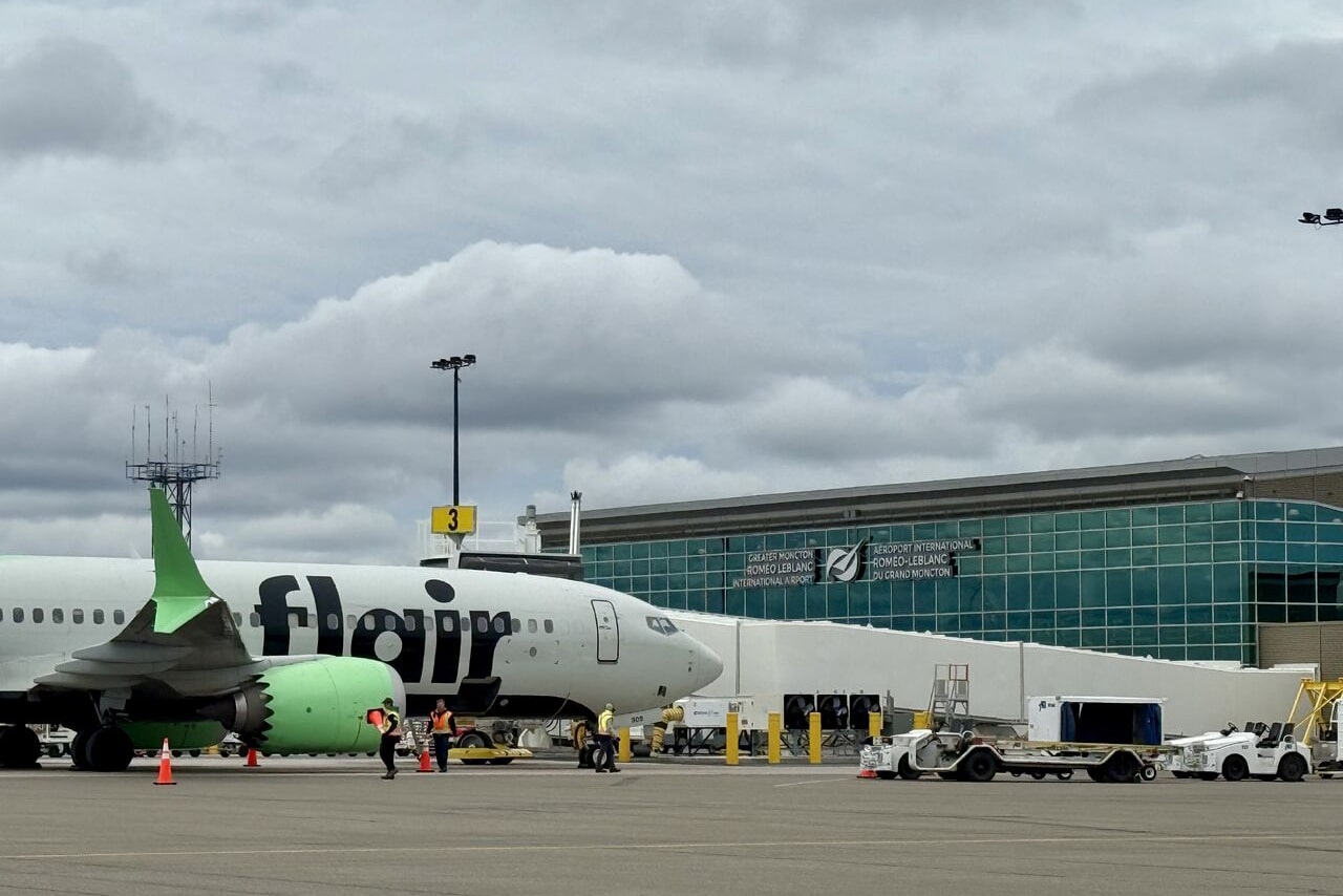 Flair Airlines aircraft parked at Moncton Airport apron with ground crew and equipment near the terminal building