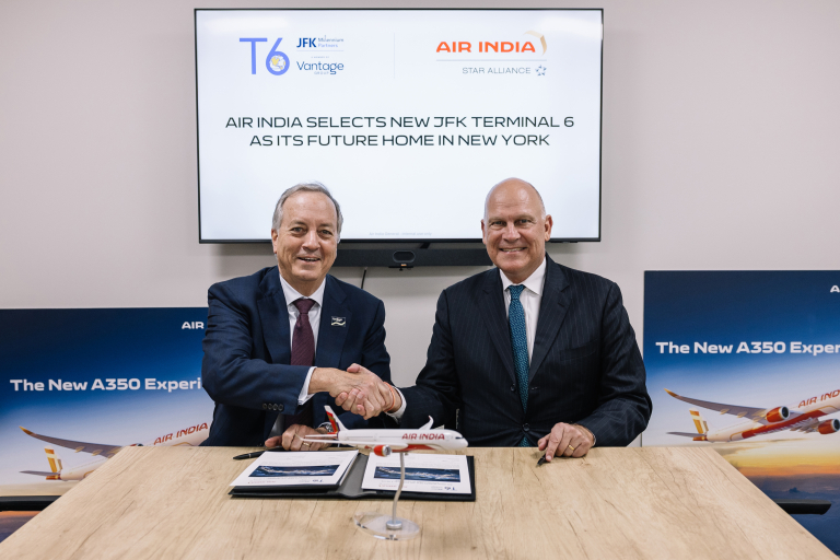 George Casey and Campbell Wilson shake hands across a conference table with an Air India A350 model between them, beneath a screen reading 'Air India Selects New JFK Terminal 6 as Its Future Home in New York,' flanked by Air India A350 branding banners.